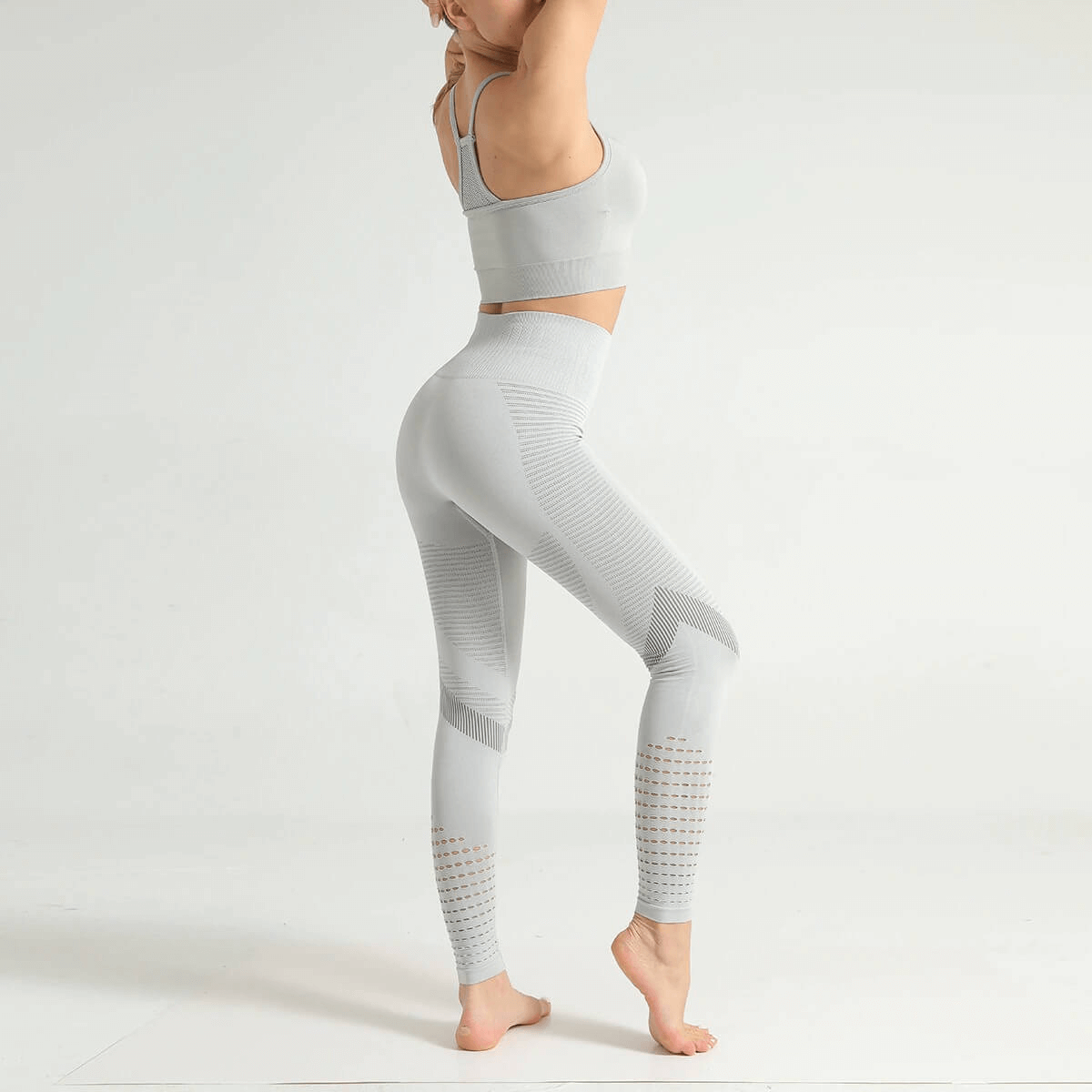 Woman wearing hollow seamless high-waisted fitness leggings in gray, showcasing side view with booty-lifting fit and breathable fabric.